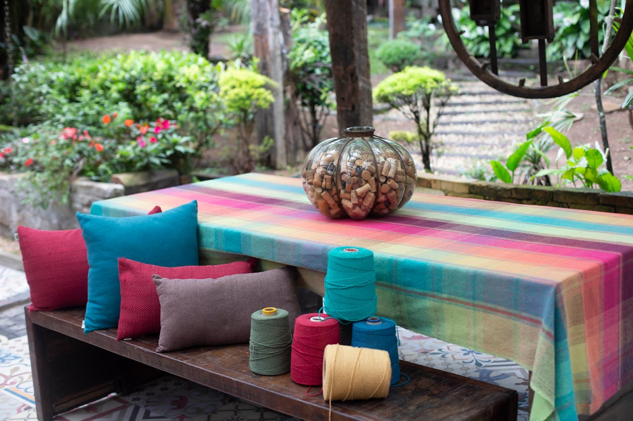 Bright garden setting featuring a colorful table, threads, and cushions.